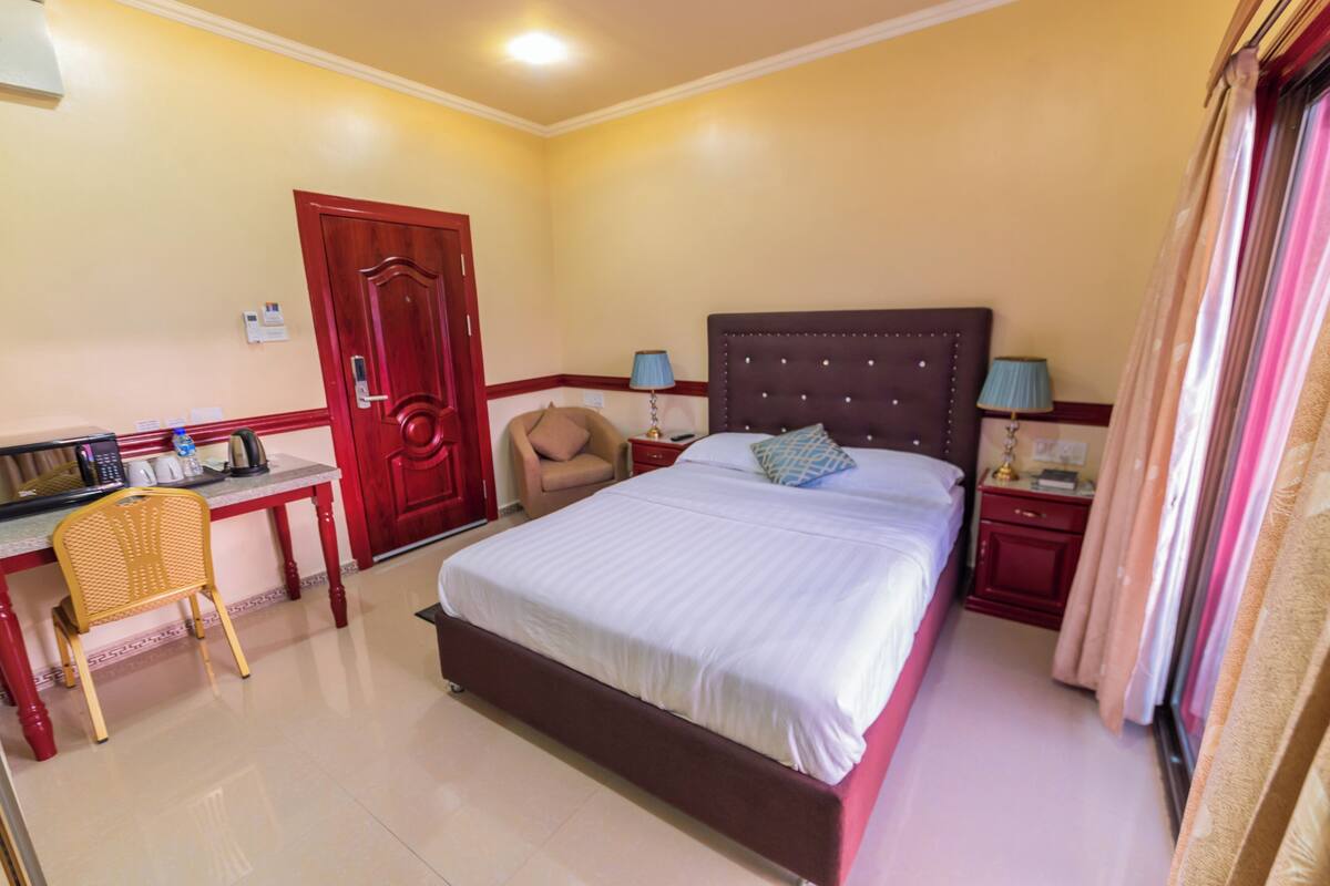 A hotel room with a bed, desk, chair, and a door.