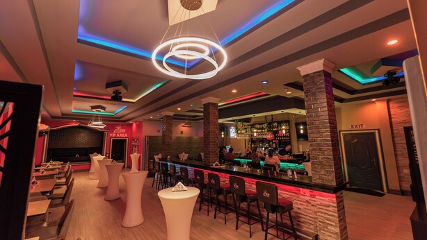 Zona de bar moderna con barra, taburetes y un área de lounge VIP con mesas y sillas.