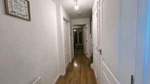 A hallway with wooden flooring, white walls, and a framed quote on the left. Doors line both sides, leading to other rooms. - Cozy Windmill House in Smethwick (Smethwick)