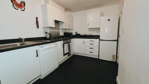 A modern kitchen with white cabinets, a black countertop, and a black tiled floor. - Cozy Windmill House in Smethwick (Smethwick)