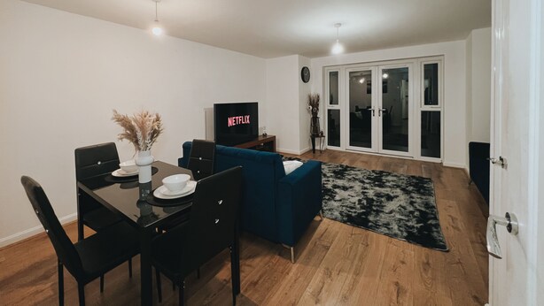 A modern living room with a dining area, a blue sofa, a flat-screen TV, and a dining table with chairs. - Cozy Windmill House in Smethwick (Smethwick)