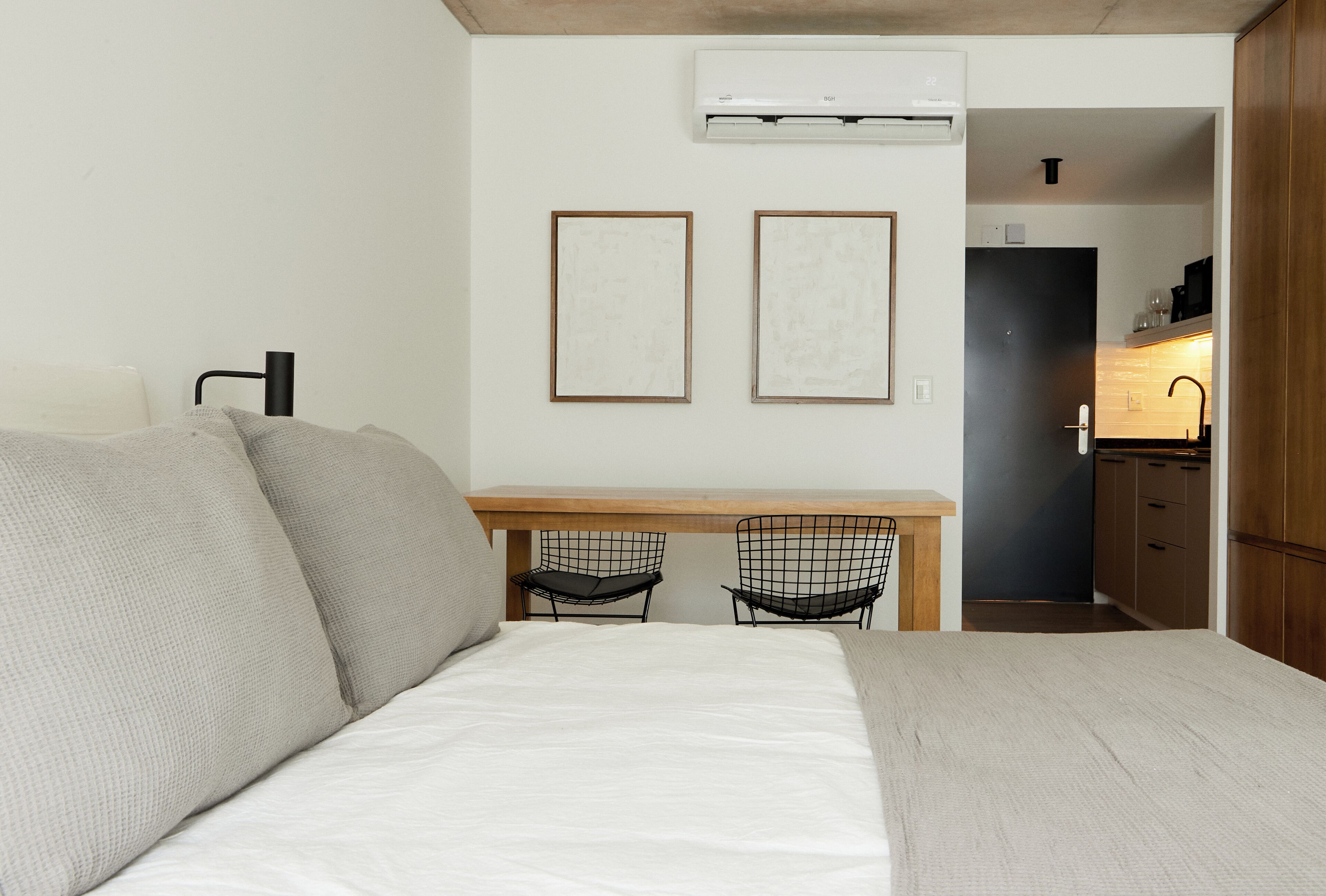 A compact room with a bed, two chairs, a small desk, and a kitchenette.