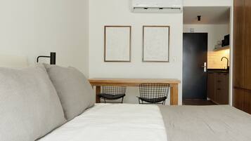 A compact room with a bed, two chairs, a small desk, and a kitchenette.