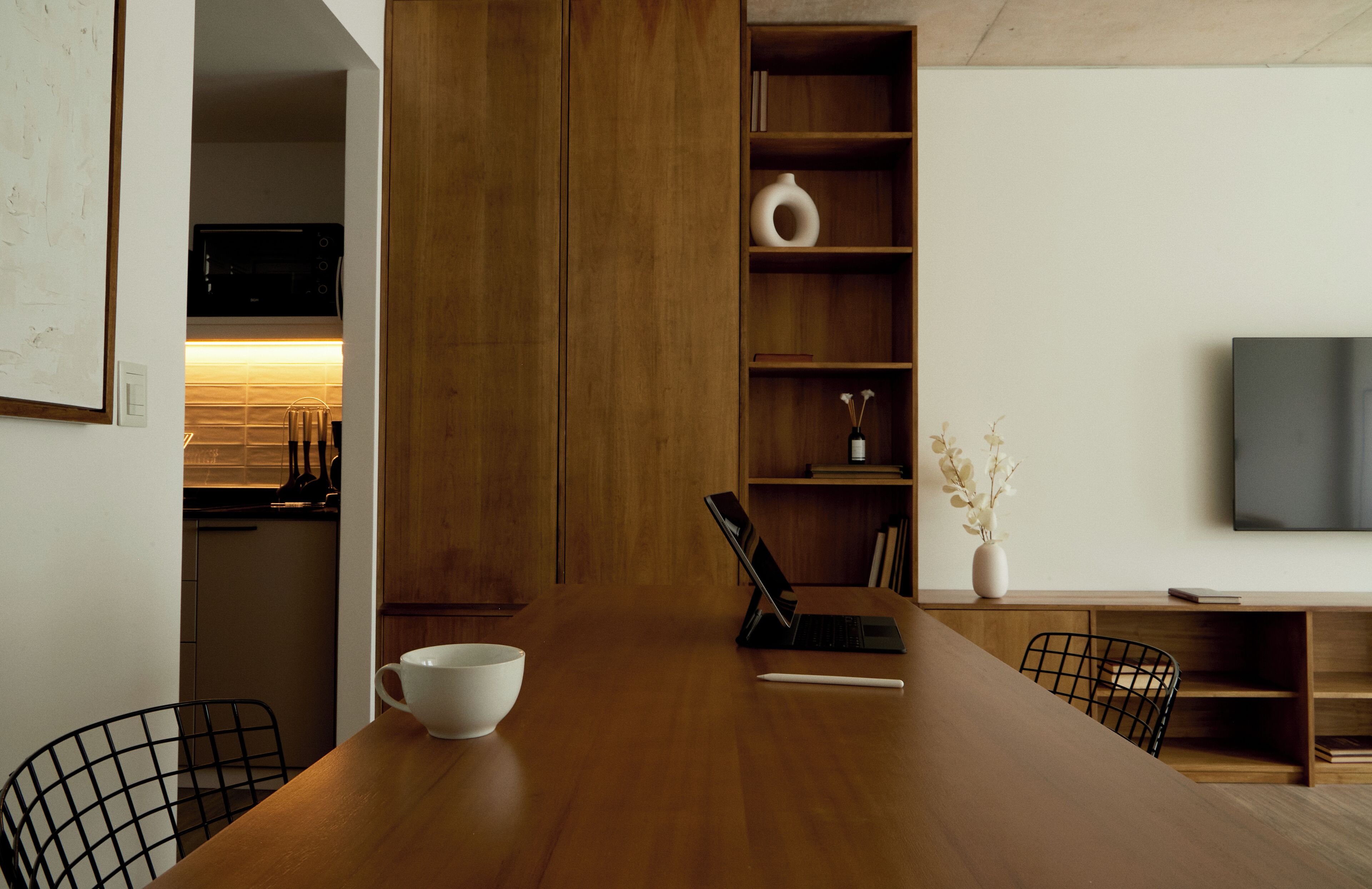 Una cocina moderna con armarios de madera, horno empotrado y un comedor con mesa de madera, sillas y un tazón blanco.