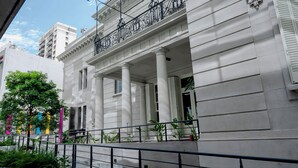 Un bâtiment de style classique, doté de colonnes blanches et d’un balcon orné de rampes en métal ouvragé.