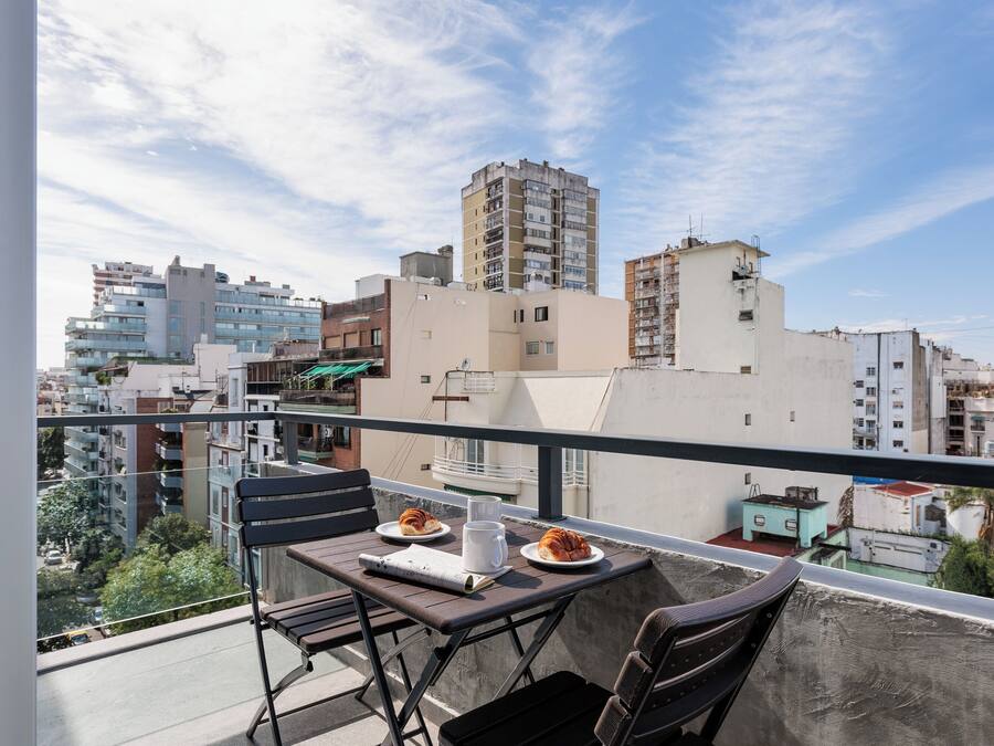 Een balkon met een tafel gedekt voor twee personen, een stoel, en uitzicht op de omgeving.