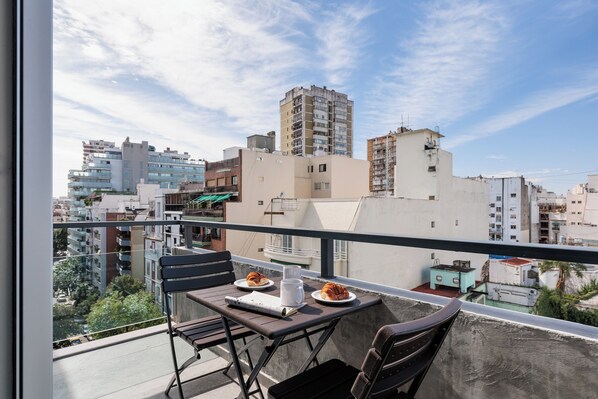 A balcony with a table set for two, a chair, and a view of surrounding buildings. - Hestia at Pasaje Calas (Buenos Aires)
