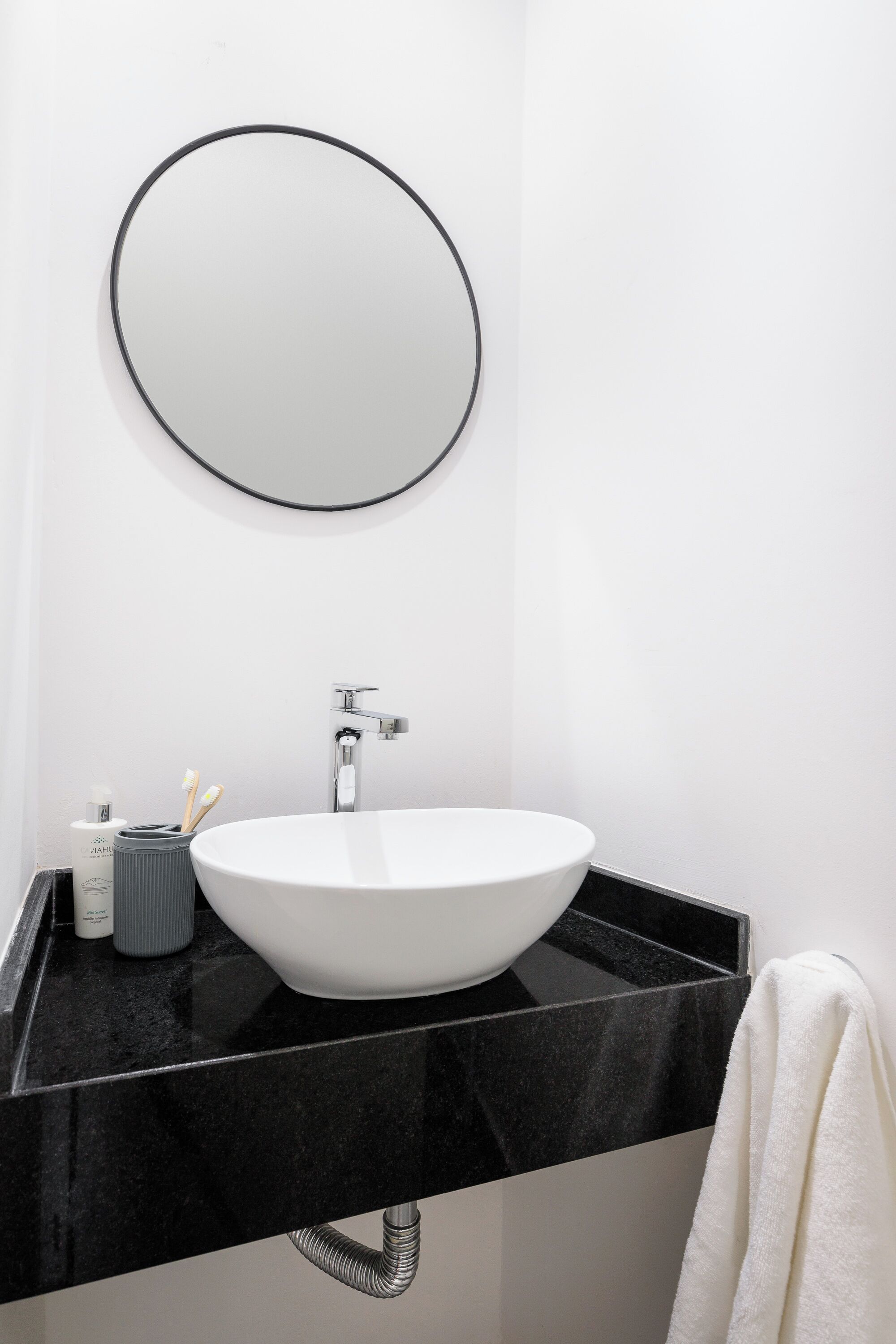 A modern bathroom with a white sink, black countertop, and a round mirror.