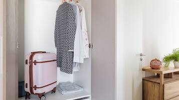 Une pièce avec un plancher en bois, une armoire blanche avec une tringle à vêtements, une valise et une petite table en bois sur laquelle est posée une plante.