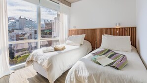 Une chambre d’hôtel moderne avec deux lits, de grandes fenêtres et une vue sur la ville.