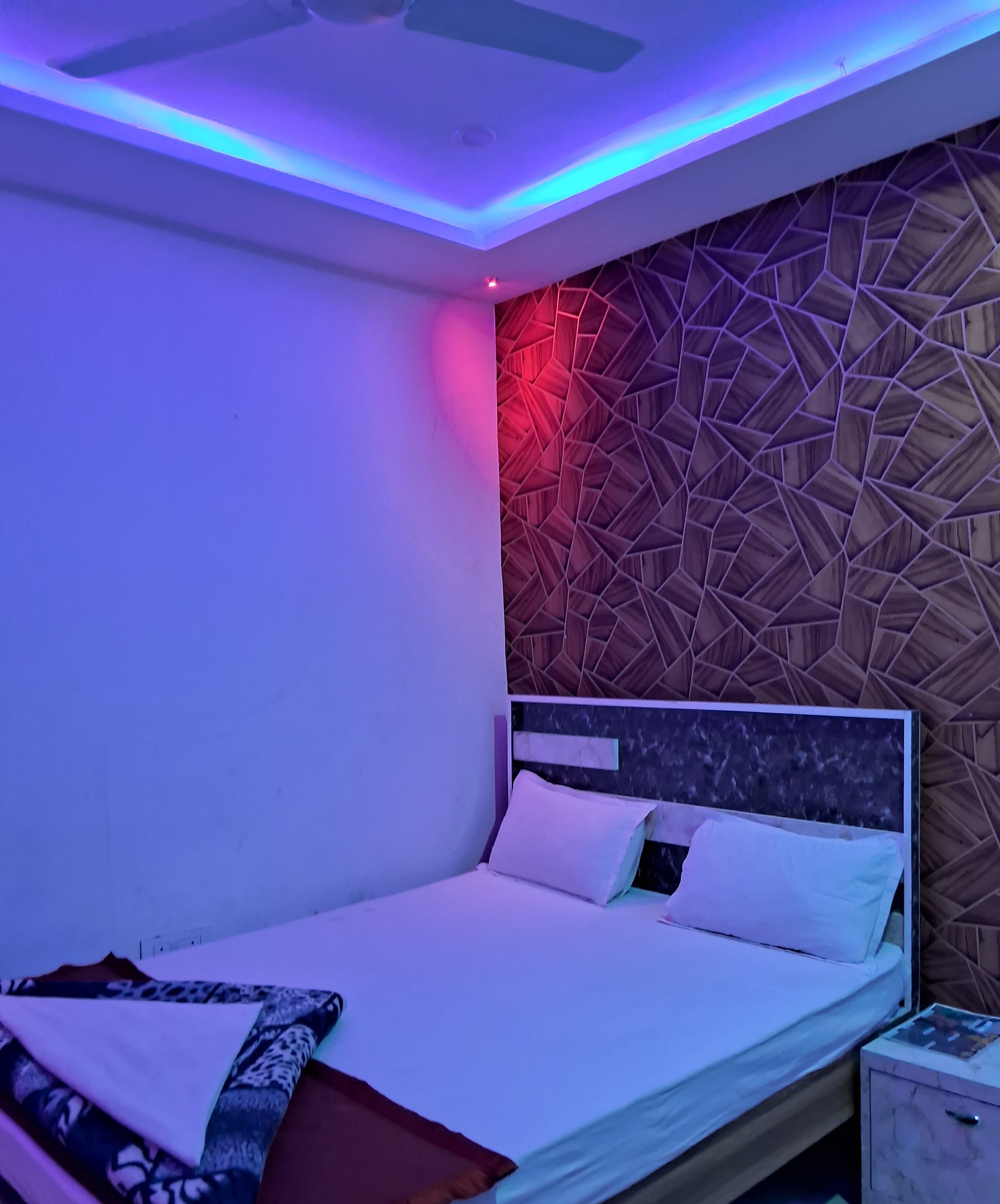 Une chambre moderne avec une tête de lit à motifs géométriques, un lit bien fait avec du linge de lit blanc et une table de chevet sur laquelle repose un magazine.