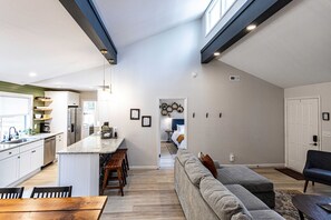 Una cocina moderna con una isla central, zona de comedor con sillas de madera, un sofá gris y una pequeña mesa.