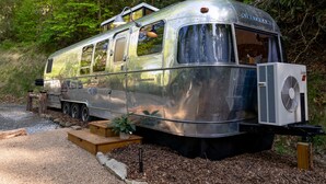 A vintage Airstream trailer with a small porch area, a fan, and a wooden bench. - Creekside Fern in Pisgah Forest (Pisgah Forest)