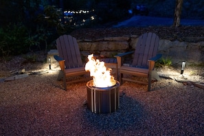 A fire pit with two Adirondack chairs around it, set on gravel.