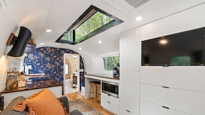 A compact RV interior with a kitchenette, a seating area with a sofa and cushions, and a large window providing natural light. - Silver Fern in Pisgah Forest (Pisgah Forest)