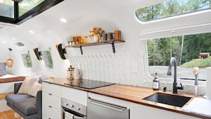 A compact kitchen with a wooden countertop, stainless steel appliances, and a window overlooking a forested area. - Silver Fern in Pisgah Forest (Pisgah Forest)