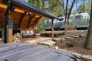 Un espacio al aire libre techado con un banco de madera y un sofá, una parrilla y una caravana estacionada al fondo.