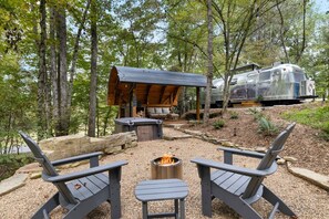 Un área de estar al aire libre de estilo rústico con sillas Adirondack, un brasero y un refugio de madera.