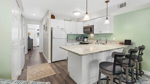 A modern kitchen with white cabinets, a granite countertop, and a built-in island with bar stools. - Close to the Boardwalk, Jolly Roger Amusement Park With a Pool! (Ocean City)