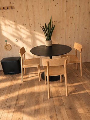 Una mesa redonda con cuatro sillas de madera, una planta en maceta y un bote de basura negro.