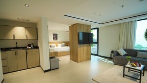 Una camera d'albergo moderna con angolo cottura, un letto con biancheria bianca, una TV a schermo piatto montata a parete, un divano e un tavolino con frutta.