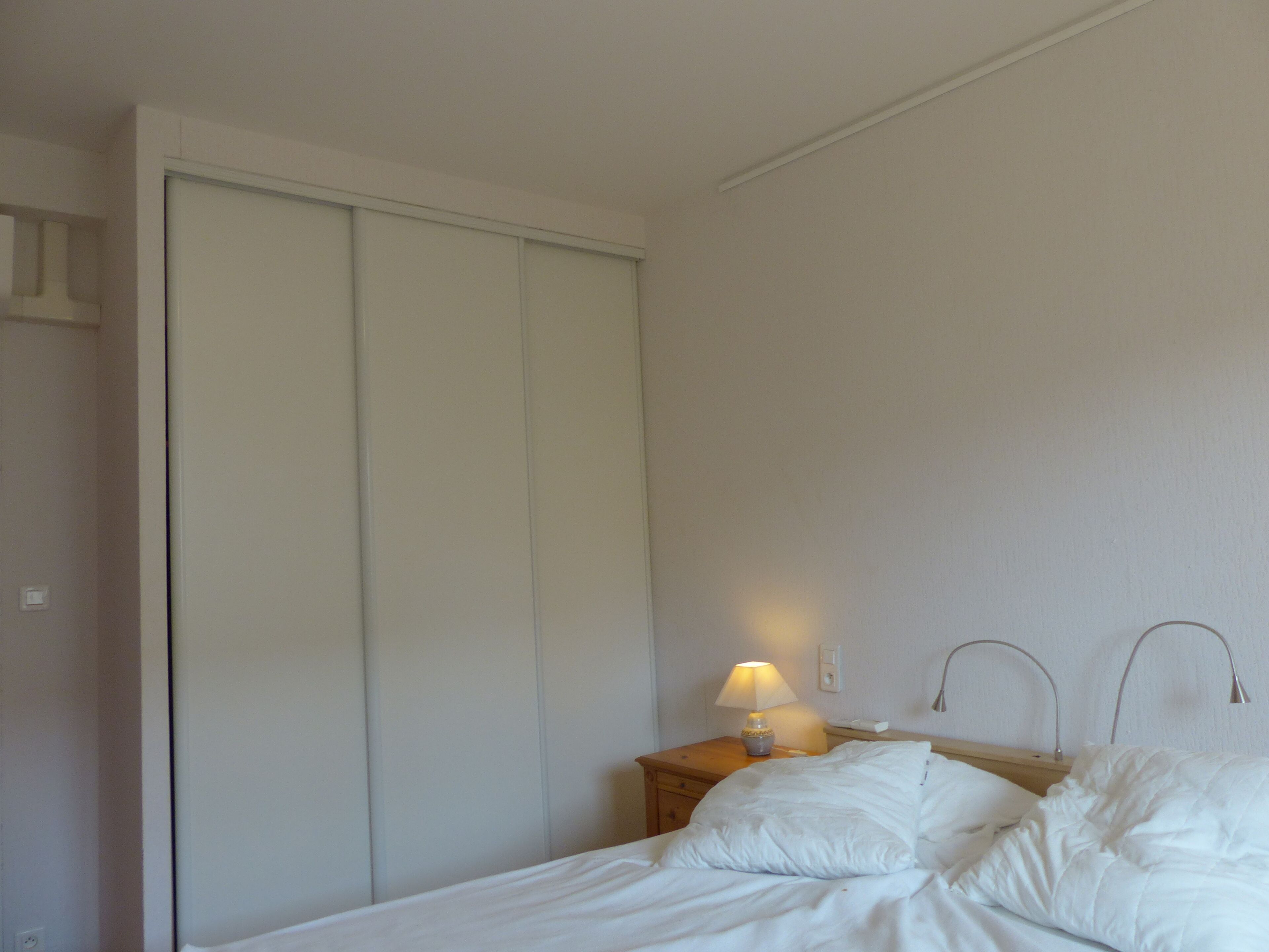 Una habitación de hotel con una cama, una mesita de noche con lámpara y un armario.