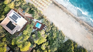 An aerial view of a beachside property with a swimming pool, sun loungers, and umbrellas.