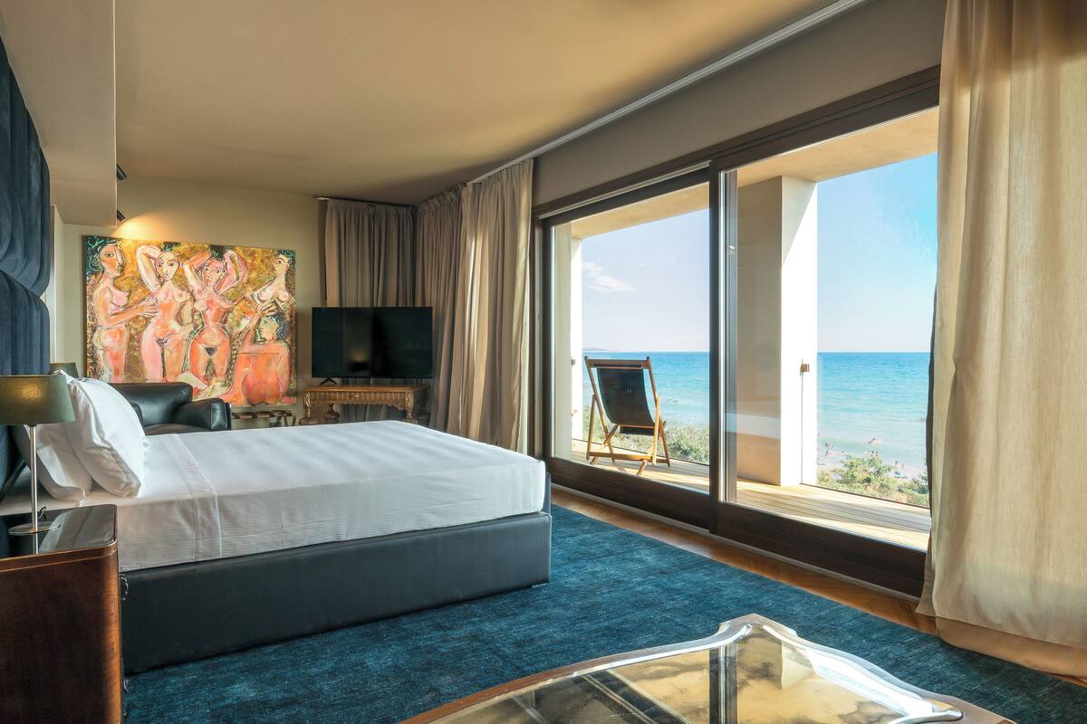 Une chambre d’hôtel avec un lit, une télévision, un tableau et une vue sur la mer.