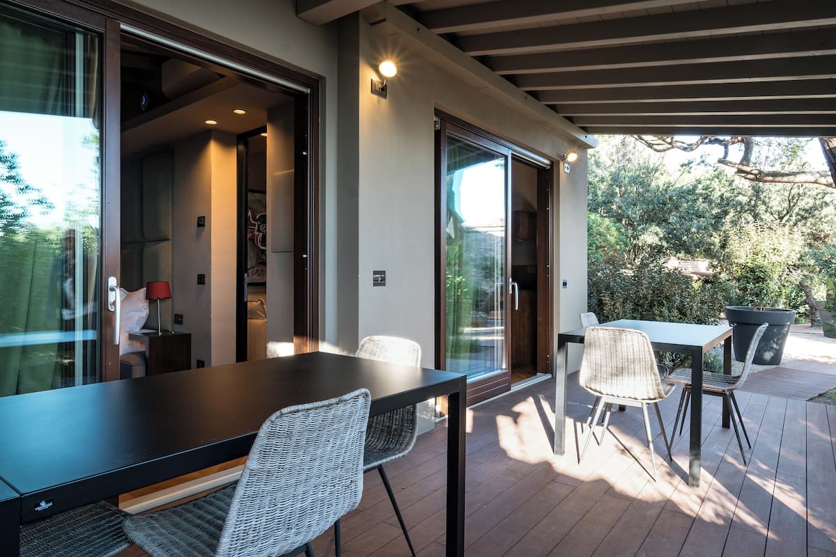 Une terrasse extérieure avec une table et des chaises, une porte vitrée donnant sur une pièce et une vue sur la verdure.