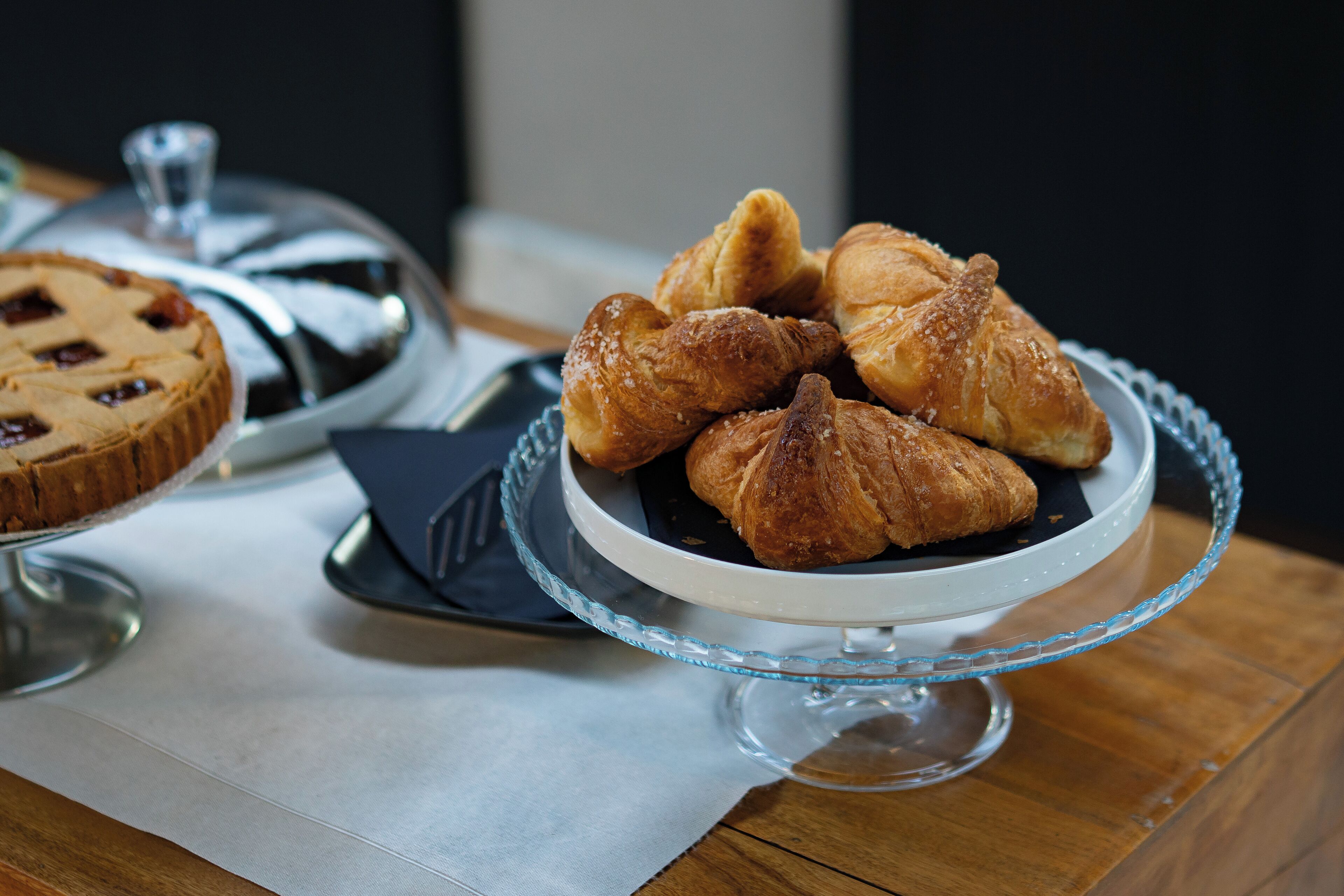 A glass cake stand with pastries and a pie on a wooden table.