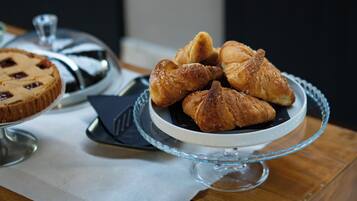 A glass cake stand with pastries and a pie on a wooden table.