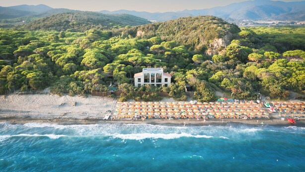 A coastal property with a beach, umbrellas, and a house surrounded by trees.