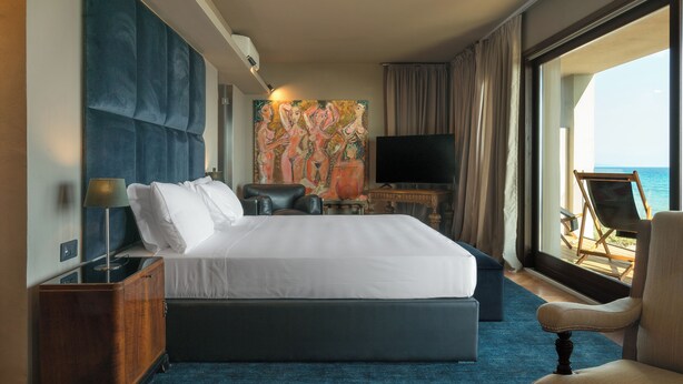A hotel room with a large bed, a television, a desk, and a view of the sea. - SUNSET VILLA  (Castiglione della Pescaia)