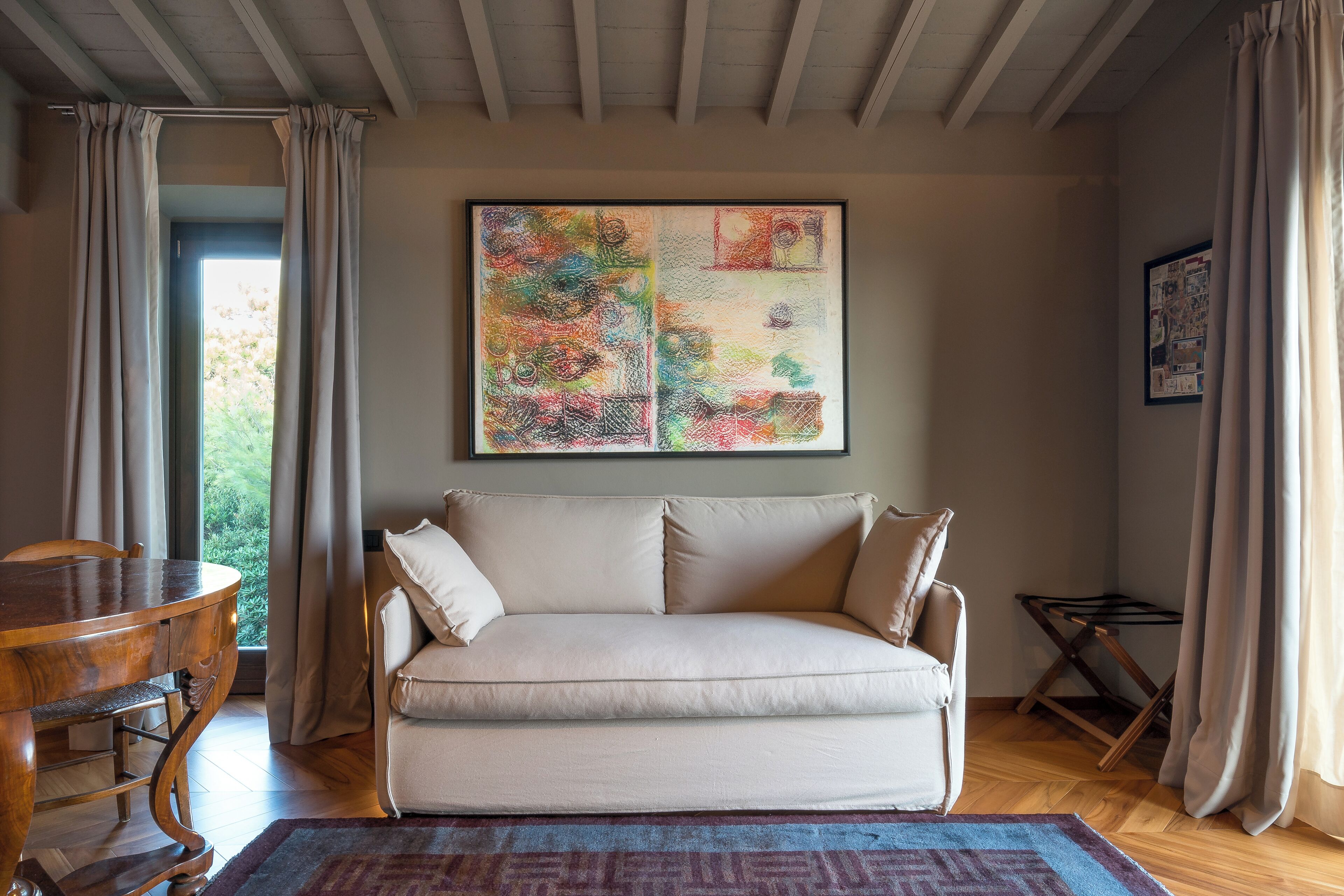 A living room with a beige sofa, a wooden dining table, and a colorful abstract painting on the wall.