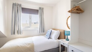 Un dormitorio ordenado con cama, mesita de noche y ventana con cortinas.