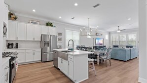 Eine moderne Küche mit weißen Schränken, einem Edelstahl-Kühlschrank und einem Essbereich mit einem blauen Sofa und einer Chandelier.