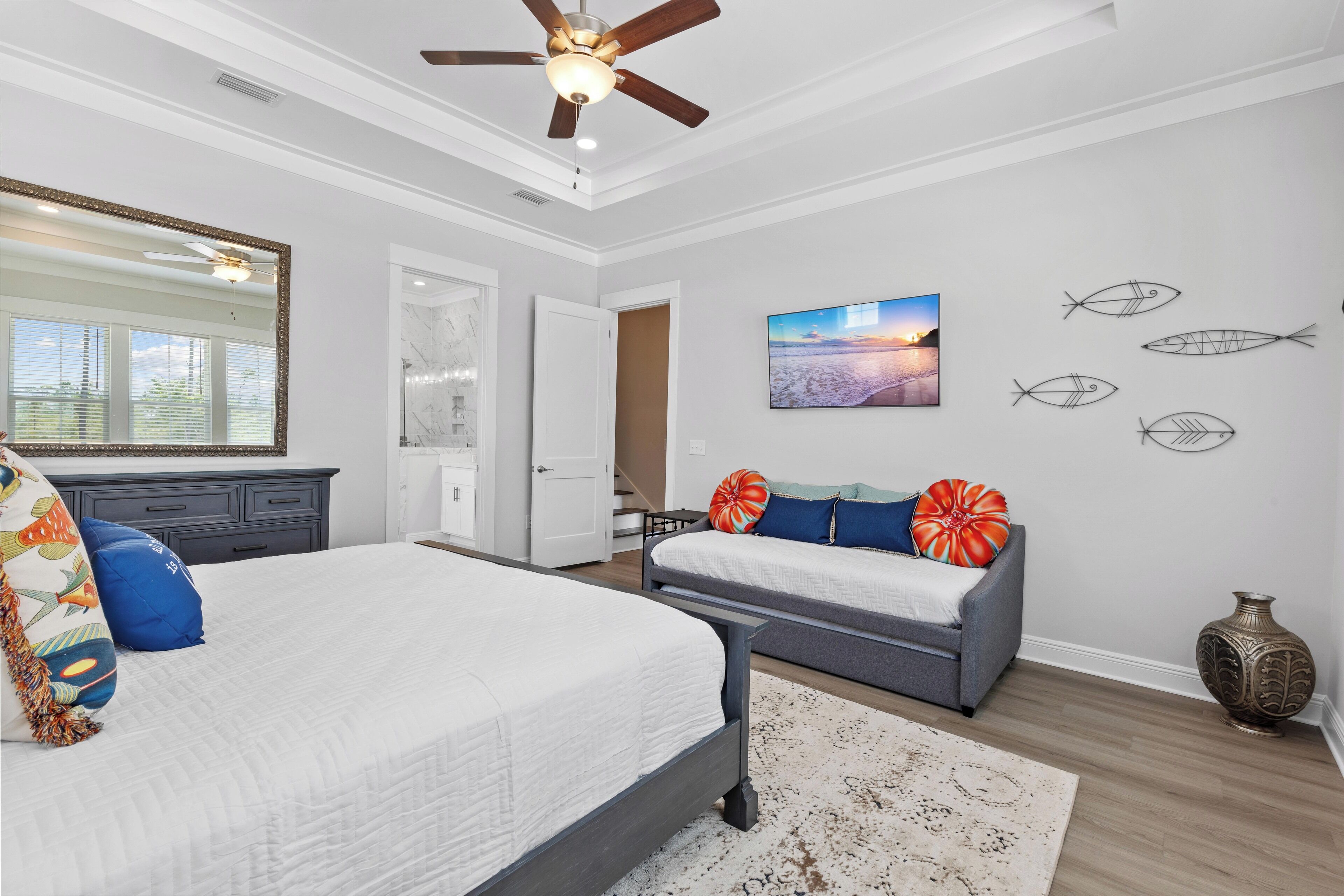 Un dormitorio con una cama, un sofá gris, un espejo grande y una pared decorada con motivos de peces.