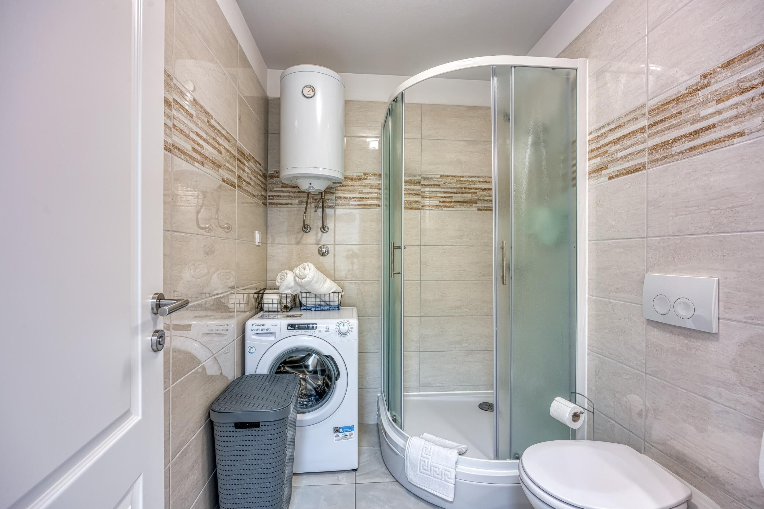 A compact bathroom with a washing machine, a glass shower enclosure, and a toilet.