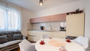 Ett modernt kök med vita och rosa skåp, ett matbord med stolar och en soffa i vardagsrummet.