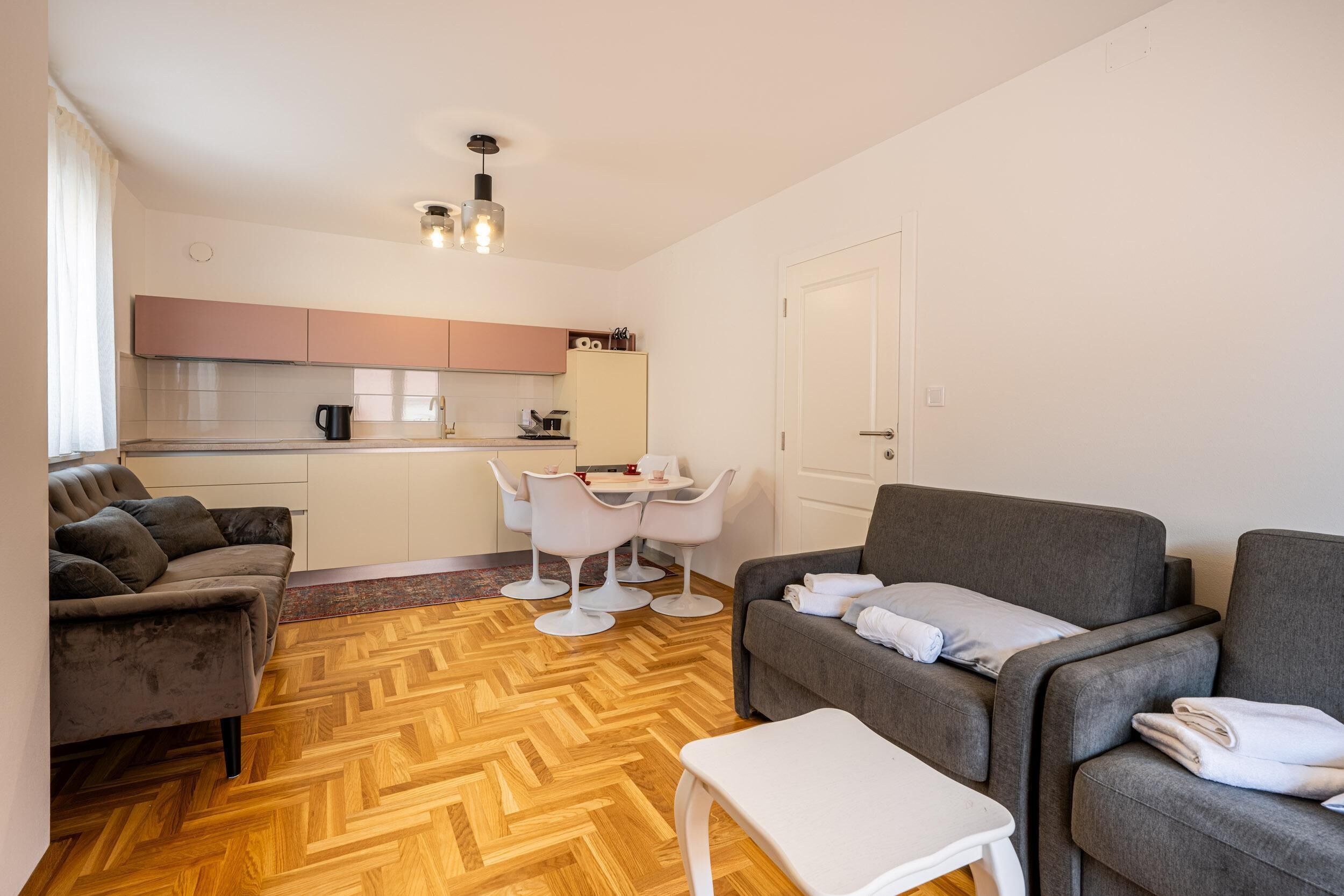 Un espace de vie compact comprenant un coin cuisine, deux canapés, une table à manger et un plancher à motifs en chevrons.