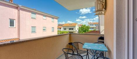 A balcony with wicker chairs and a table, overlooking neighboring buildings and a clear sky.