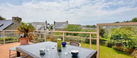 A patio with a table set for two, a potted plant, and a view of the surrounding neighborhood.