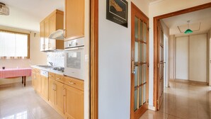 A kitchen with wooden cabinets, a tiled backsplash, and a window with a checkered tablecloth. - House for 6 with a view of the port of Dahouët (Pléneuf-Val-André)