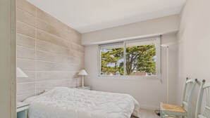 A bedroom with a bed, bedside tables, a window with a view of trees, and two chairs. - Appartment for 4 in the heart of La Baule (La Baule-Escoublac)