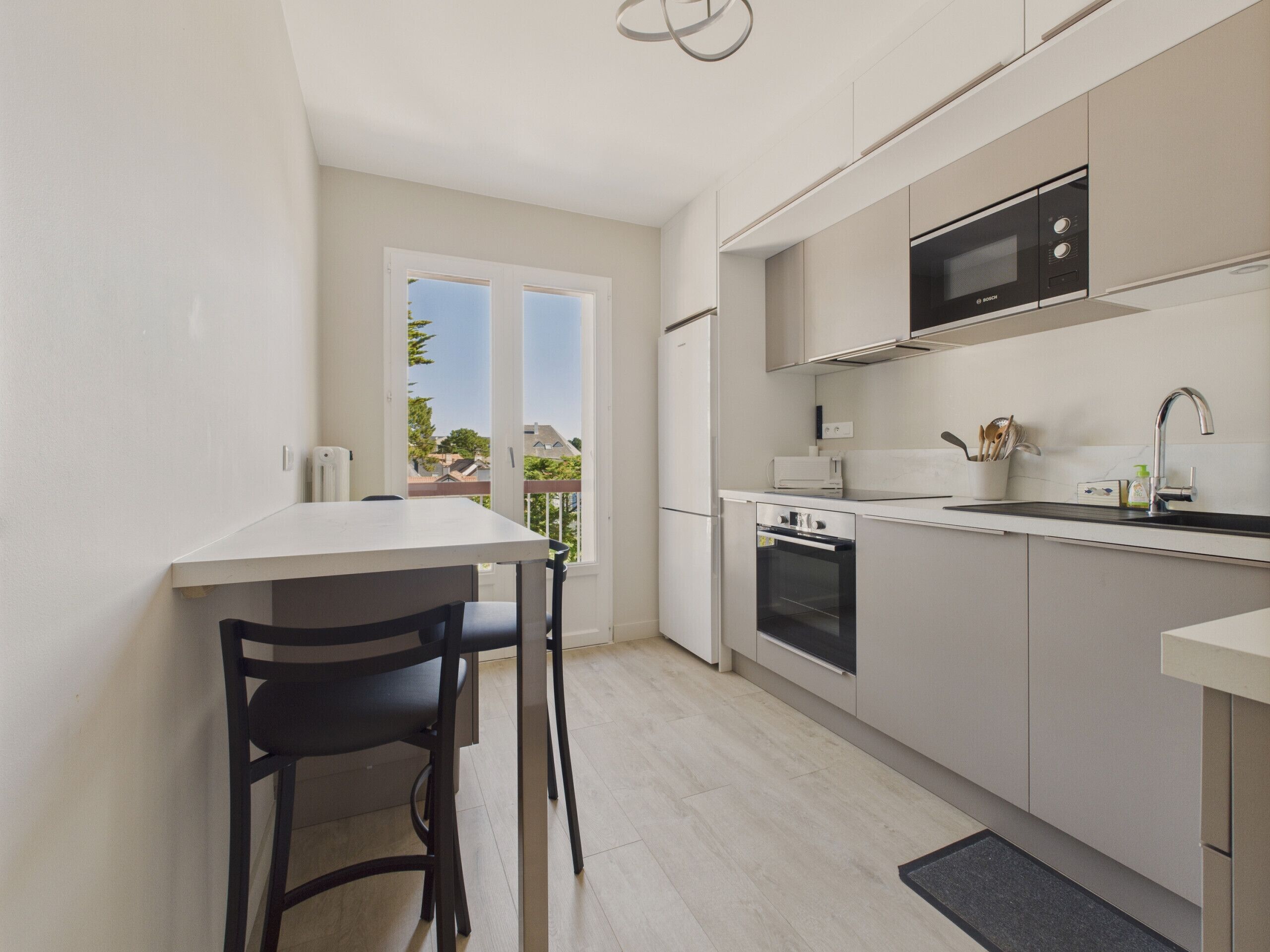 A modern kitchen with a built-in oven, microwave, and sink. There is a dining area with a table and chairs.