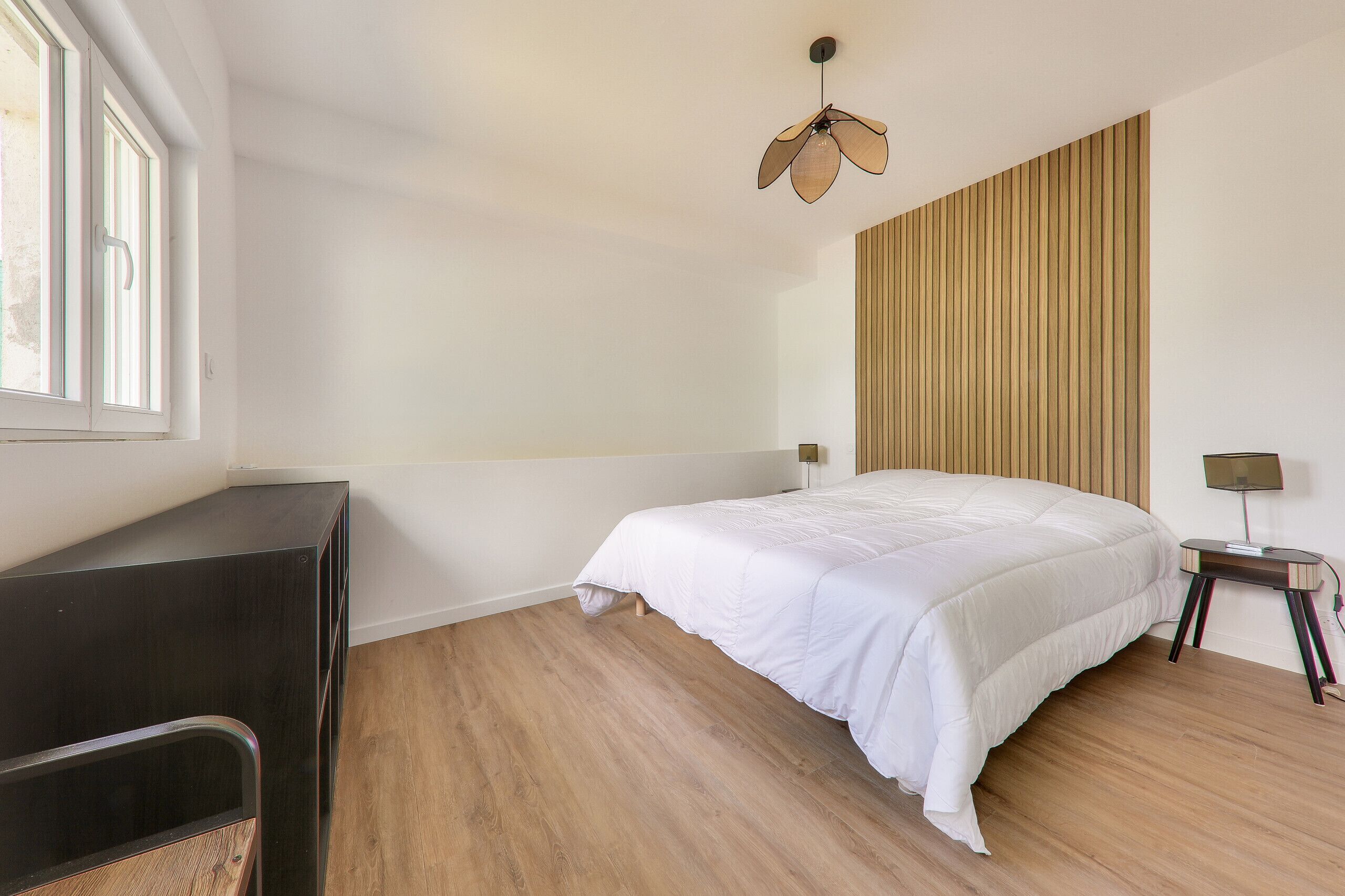 Een slaapkamer met een bed, bureau, lamp en raam.