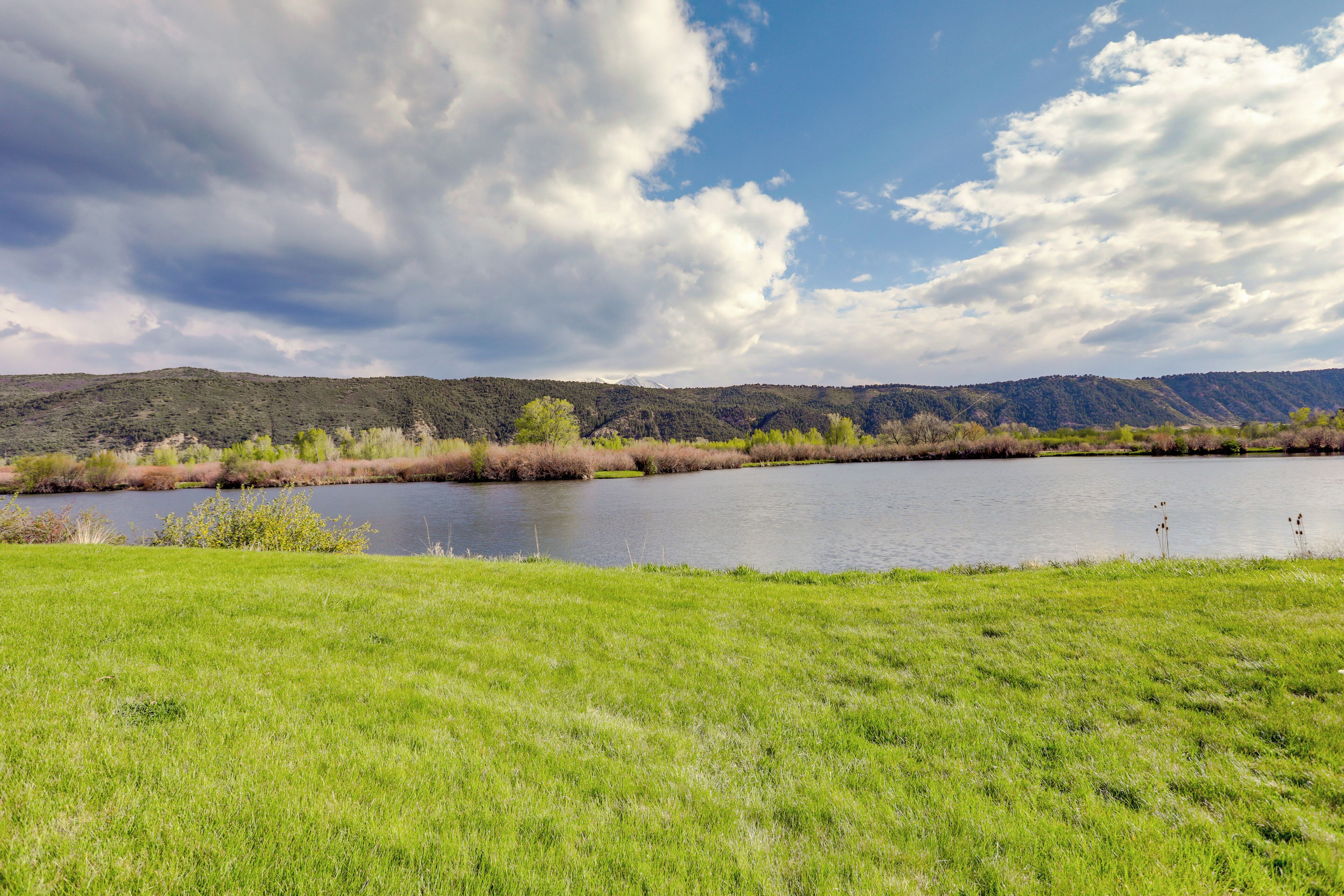 Ein grasbewachsenes Feld mit einem Gewässer und Hügeln im Hintergrund.