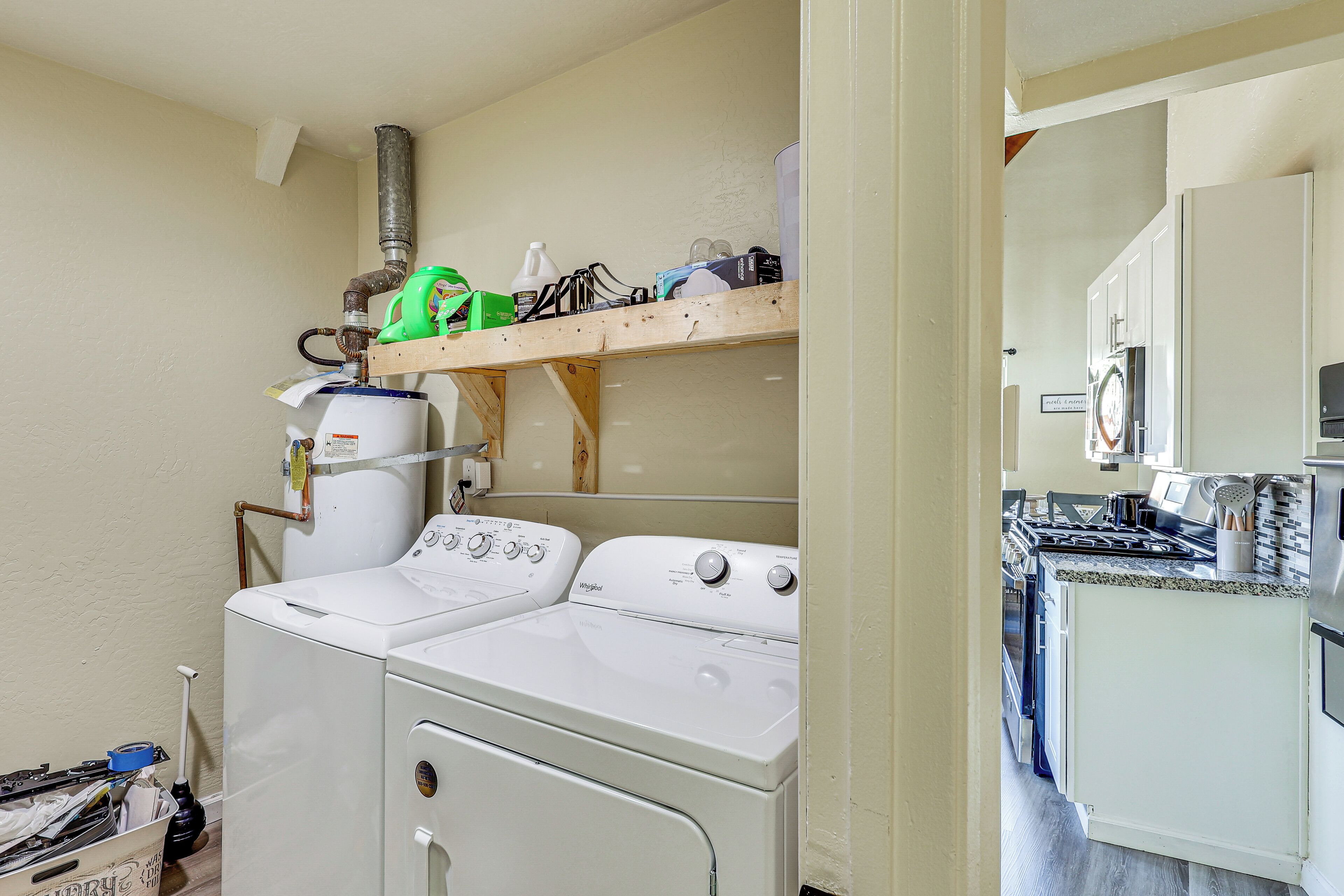 Une buanderie équipée de deux machines à laver à chargement frontal, d’un sèche-linge et d’une étagère en bois située au-dessus des sèche-linge, où sont rangés divers objets.