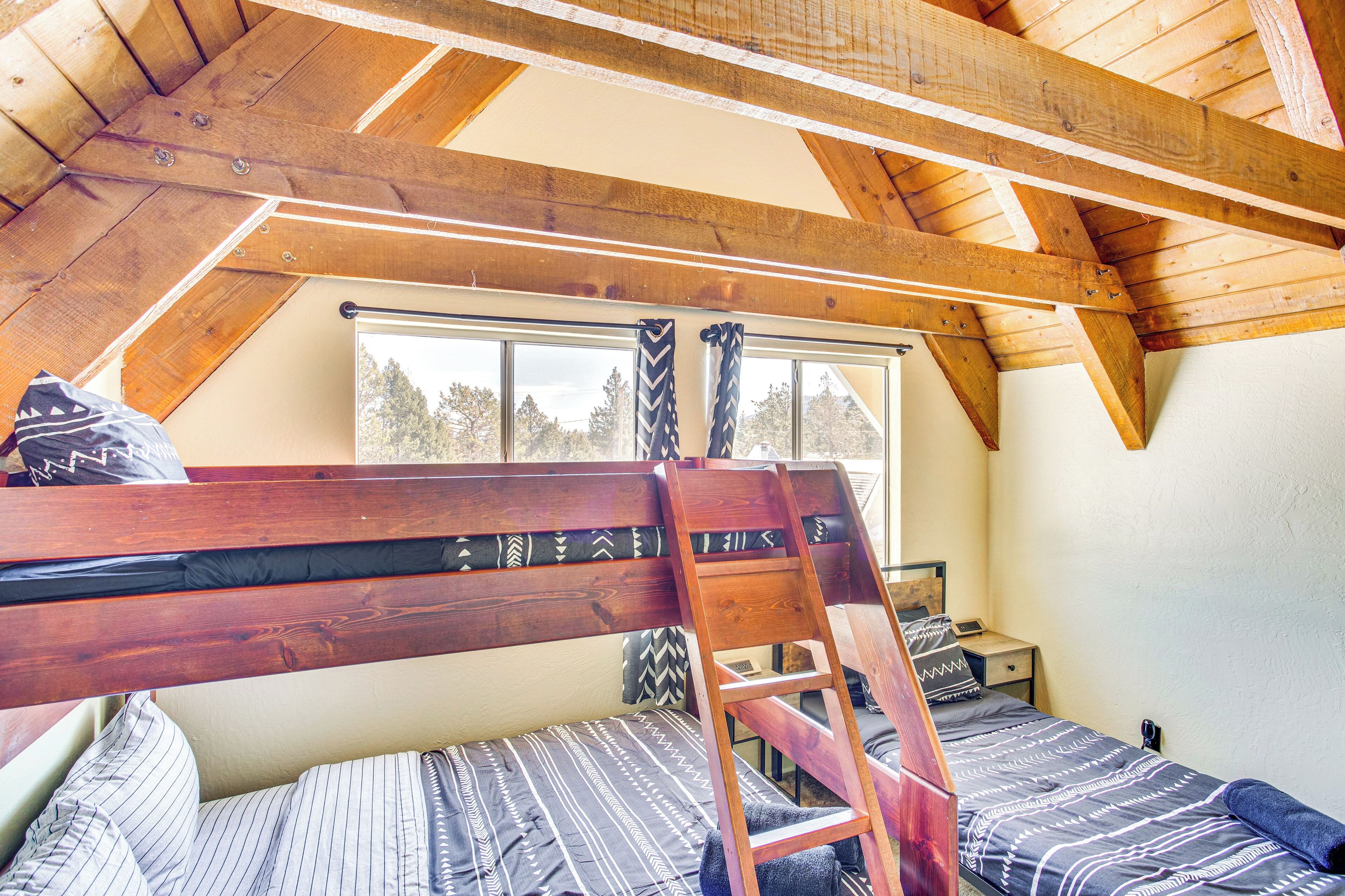 A loft bedroom with a wooden ceiling, a bunk bed, a ladder, and a window with curtains.