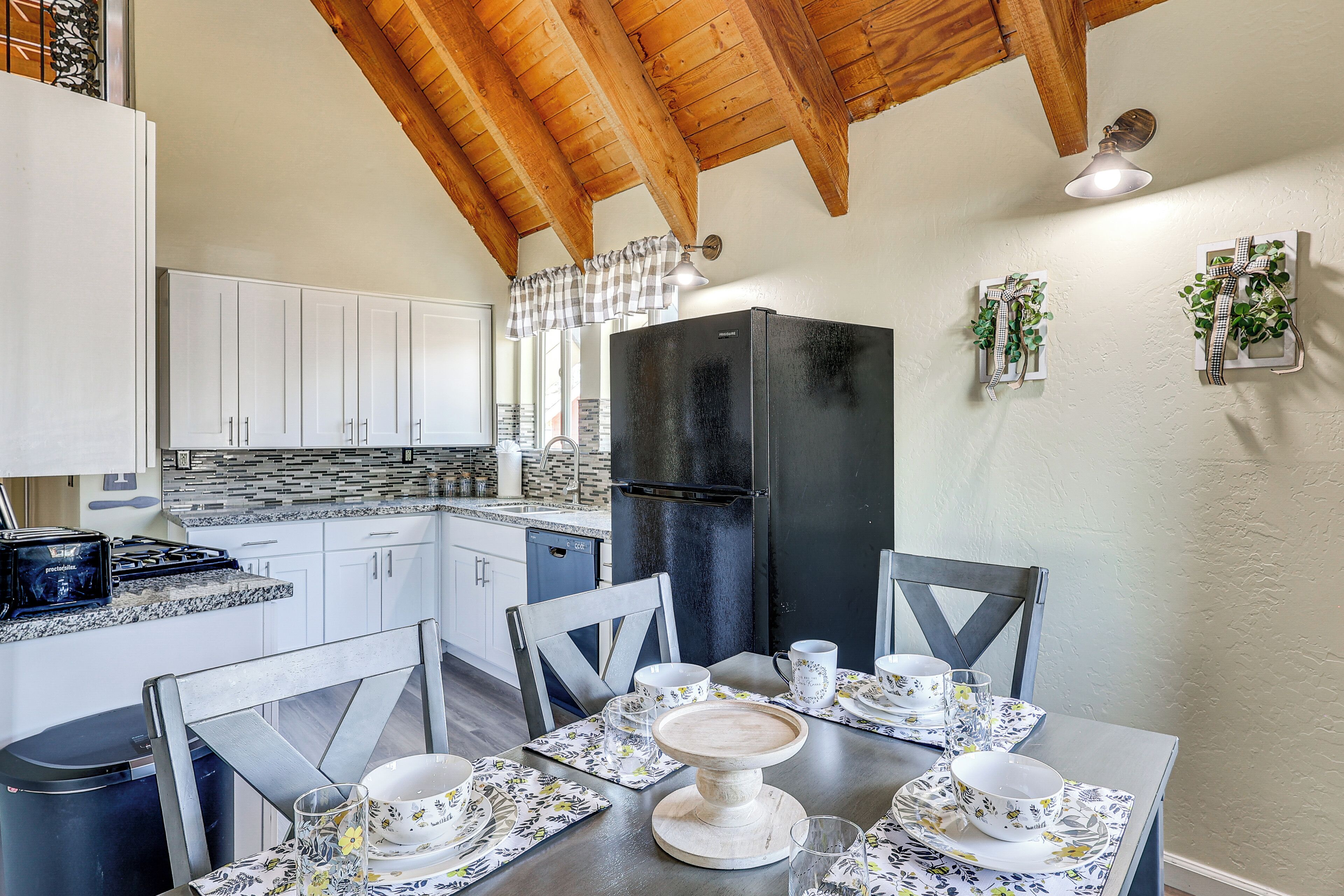 Una cocina con armarios blancos, un refrigerador negro y una mesa de comedor con vajilla estampada.